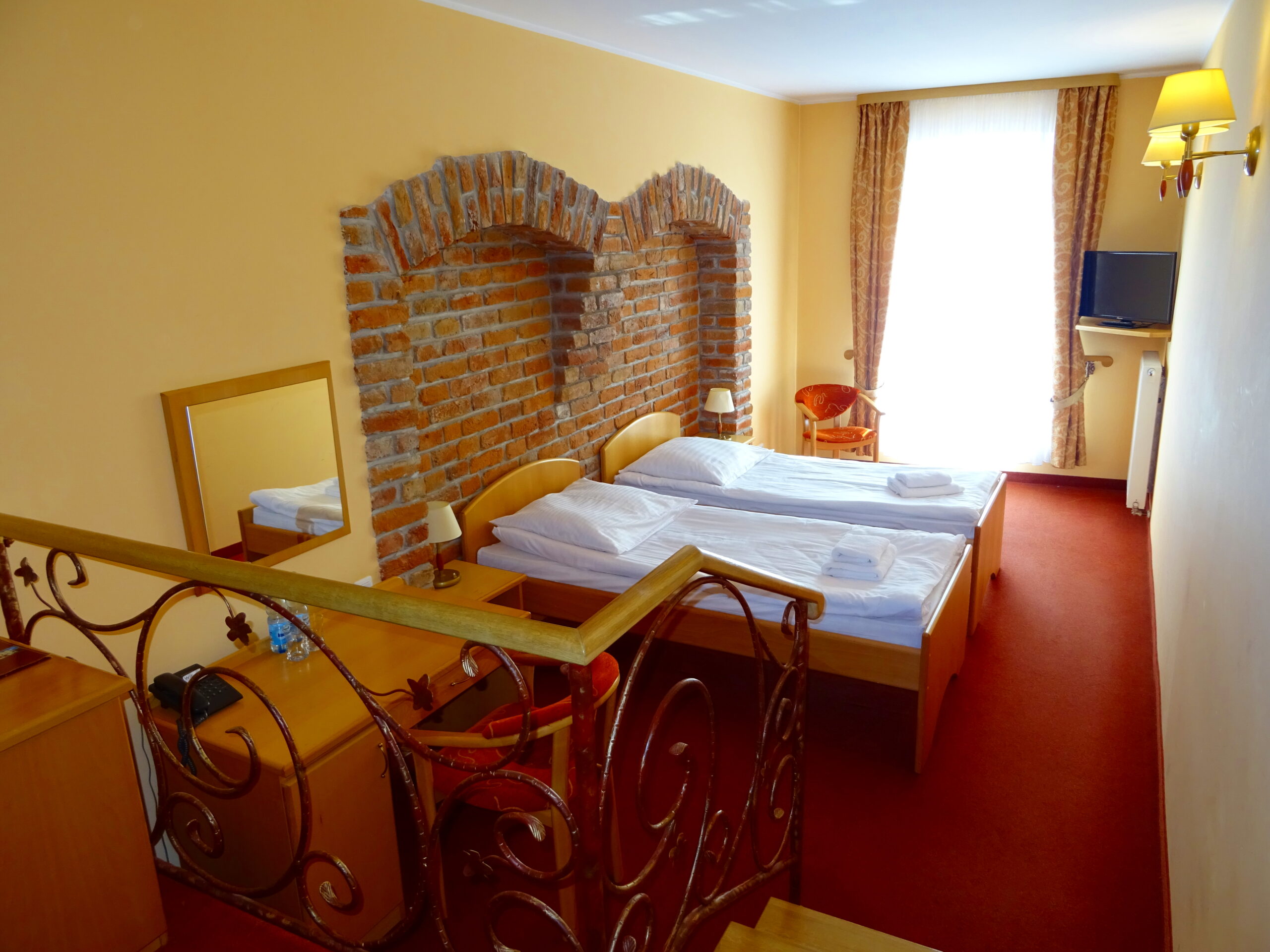 Hotel Bartis twin room with two single beds, exposed brick arches, a bright window and red carpet.