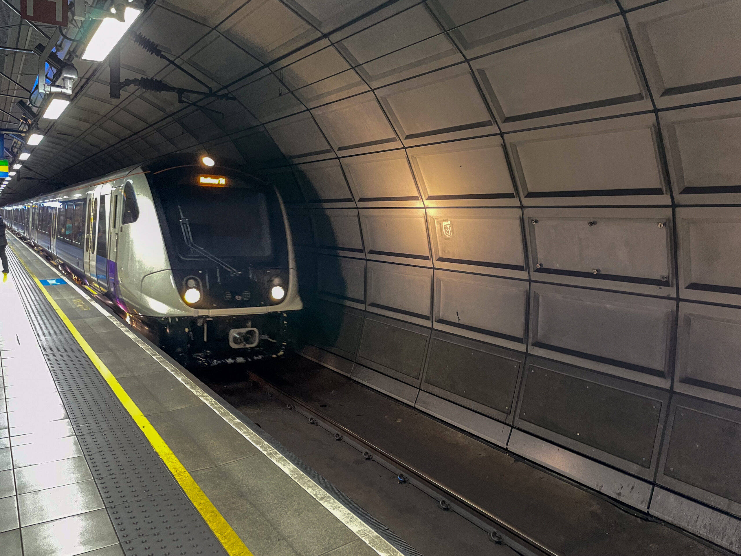 Silver and purple Elizabeth line train beside the underground platform at Heathrow Terminals 2 & 3.
