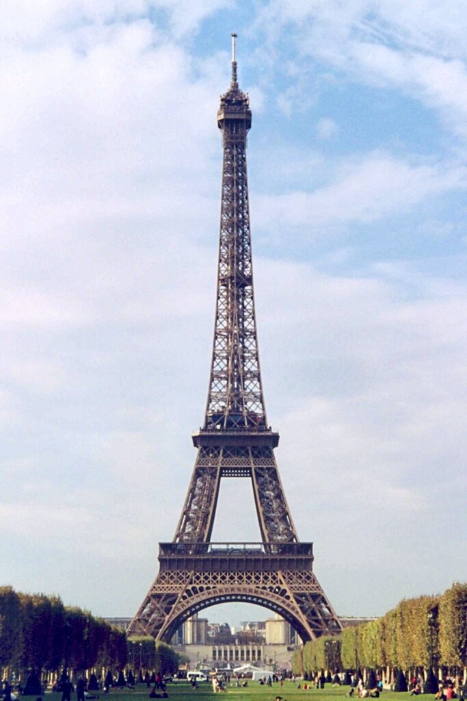 Daytime view of the Eiffel Tower rising above trees in Champ de Mars.