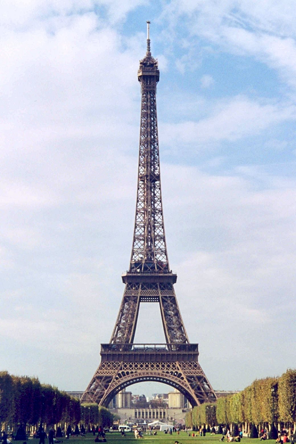 Daytime view of the Eiffel Tower rising above trees in Champ de Mars.