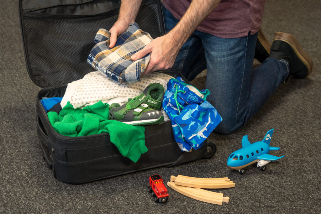 A father packing a child’s luggage for a family vacation.